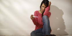 Sad Asian girl looking at pregnancy test sitting on floor